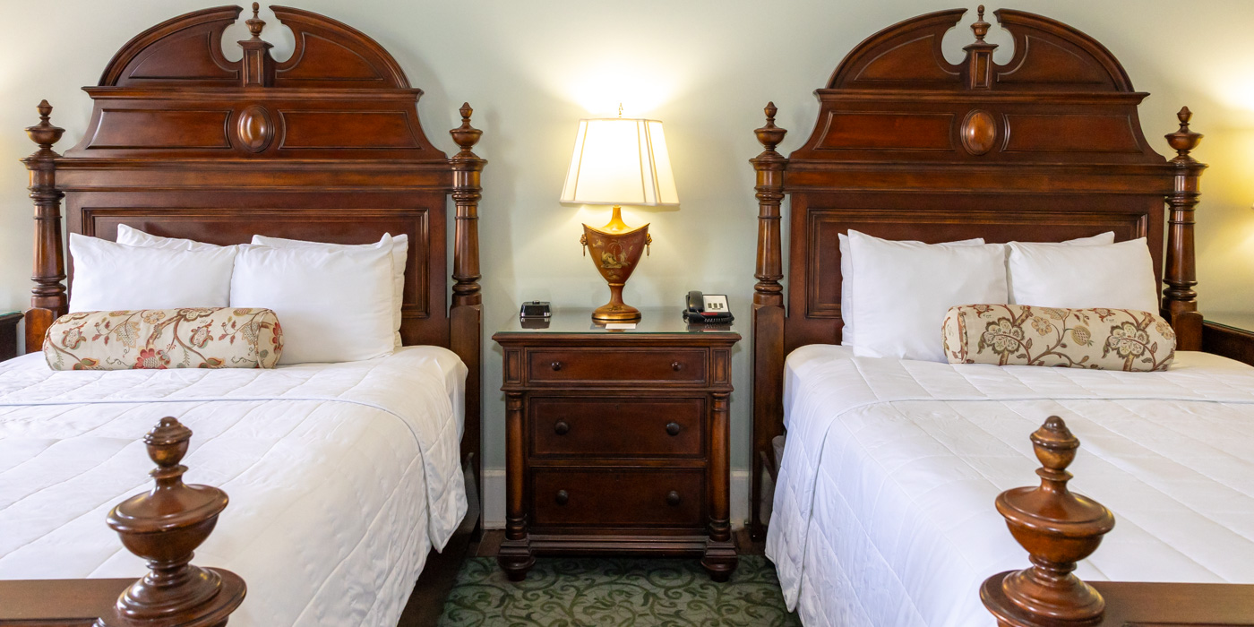 two beds with white pillows and a lamp on a nightstand